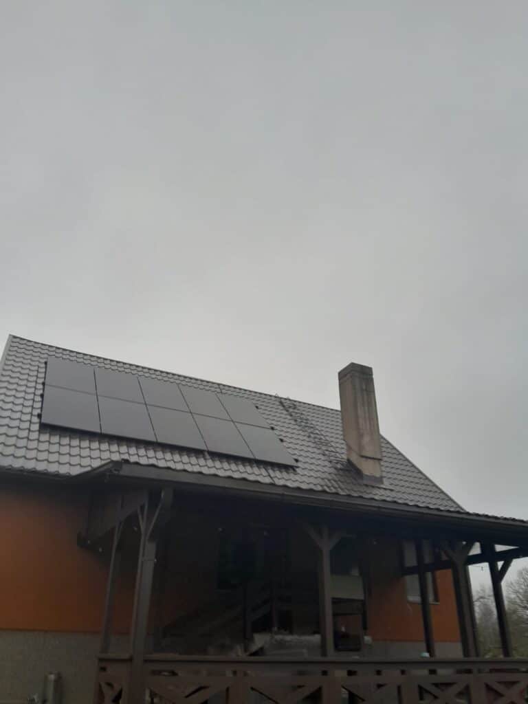 Māja ar saules paneļiem uz jumta. Brūns jumts un skurstenis. Mākoņaina diena.