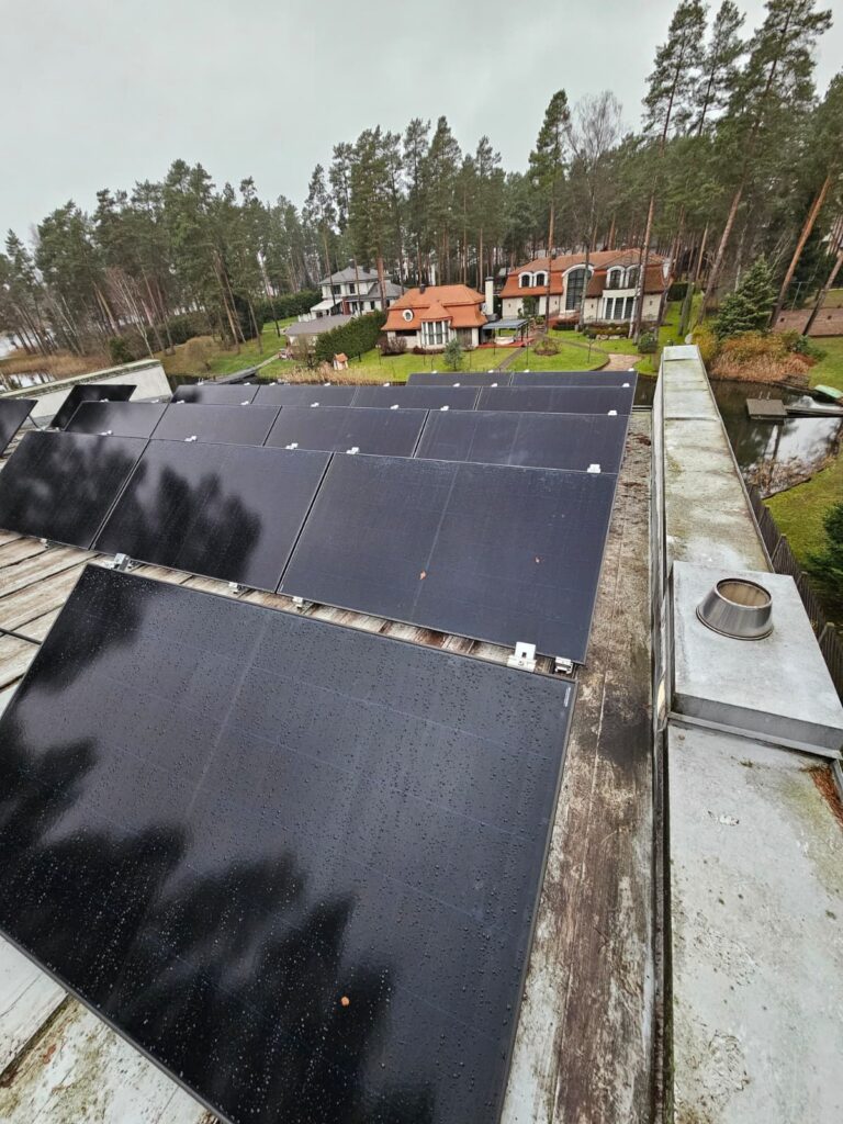 Saules paneļi uz jumta ar skatu uz mājām pie ezera. Lietaina diena.