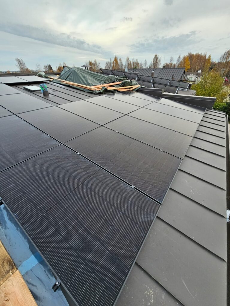 Saules paneļi uz metāla jumta uzstādīšanas procesā. Jauns, melns jumts ar solāro sistēmu. Mājas ainava fonā.