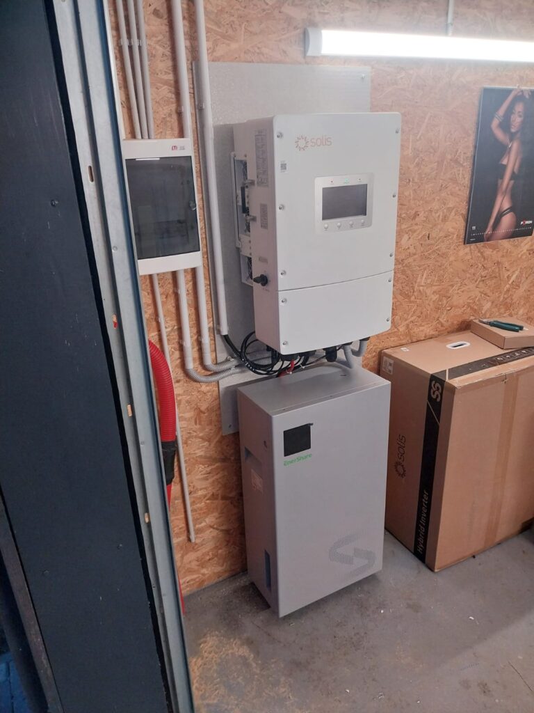 Saules paneļu invertors Solis ar Enerstone akumulatoru pie sienas. Elektroinstalācija un kabeļi redzami.