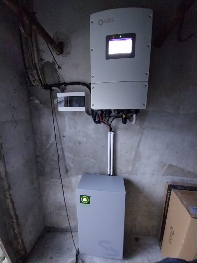 Solis hibrīda invertors ar akumulatoru, uzstādīts iekštelpās. Zaļš logotips uz akumulatora.