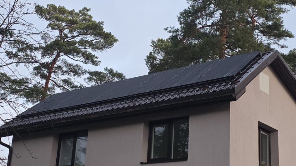 Māja ar melnu jumtu un tumšiem logiem pretī zaļiem kokiem. Mūsdienīga arhitektūra, mierīga ainava.