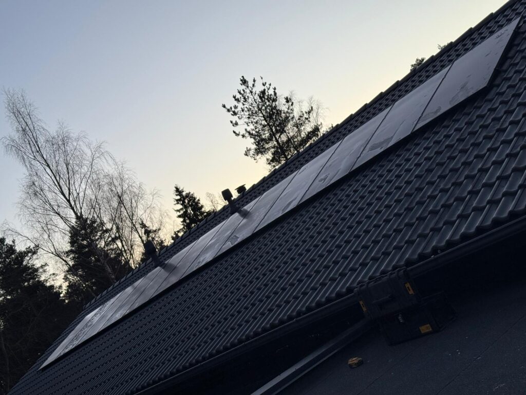 Saules paneļi uz jumta ar tumšiem dakstiņiem, koki fonā. Energoefektivitāte.