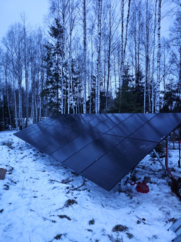 Saules paneļi sniegā, meža fonā. Ziemas ainava ar saules enerģijas iekārtu.