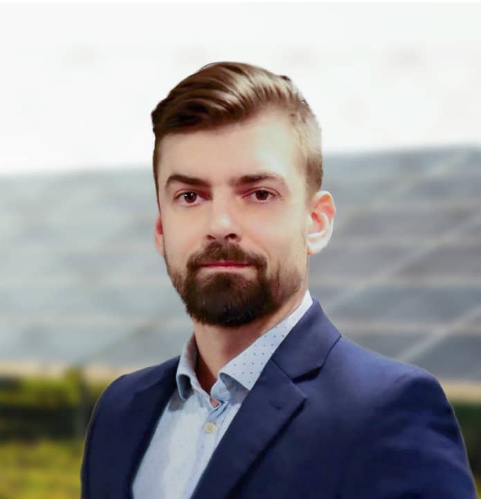 Vīrietis uzvalkā ar saules paneļiem fonā. Enerģētikas speciālists, zaļā enerģija.